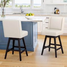 two white stools sit in front of a kitchen island with fruit on the counter