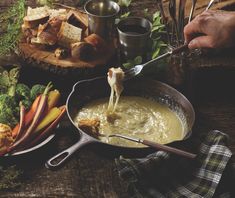 a person is dipping broccoli into a sauce in a skillet on a wooden table