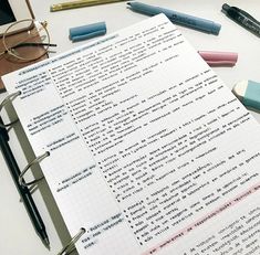 an open notebook sitting on top of a table filled with pens and writing utensils