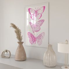 three pink butterflies on a white wall in a room with a lamp and vases