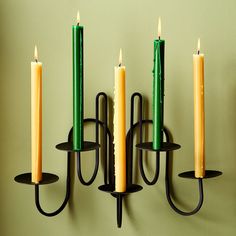 three candles are hanging on the wall next to two black holders with green and yellow candles