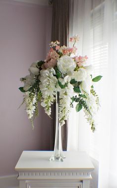 a vase filled with white and pink flowers sitting on top of a table next to a window