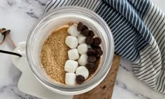 a cup filled with marshmallows and chocolate chips on top of a cutting board