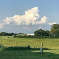 an open field with trees and clouds in the background