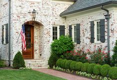 a brick house with an american flag hanging on the front door and landscaping around it