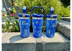 three blue tumblers sitting next to each other in front of some bushes and flowers