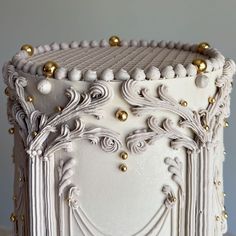 a white cake with gold decorations on it's sides and frosting around the edges