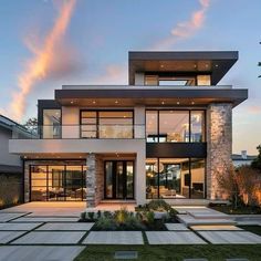 a large modern house with lots of windows and grass in the front yard at dusk