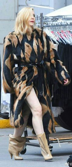 a woman is walking down the street wearing boots and a fur coat with an animal print pattern on it