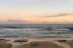 an ocean view with waves coming in to shore and the sun setting on the horizon