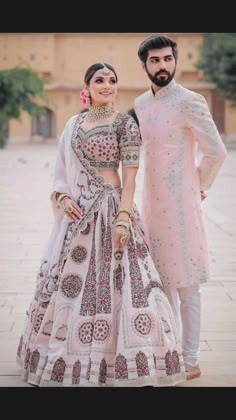 two people standing next to each other in wedding outfits, one wearing a pink lehenga