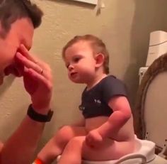 a man brushing his teeth with a toddler sitting on the toilet