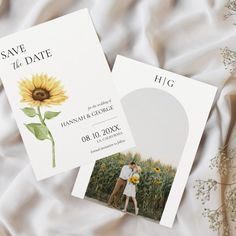 two save the dates cards with sunflowers on them next to white sheets and flowers