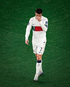 a man standing on top of a soccer field holding his hands to his face while wearing a white uniform