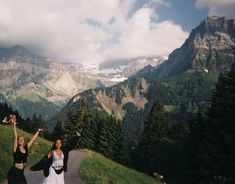 two women standing on the side of a road with their arms in the air and mountains behind them