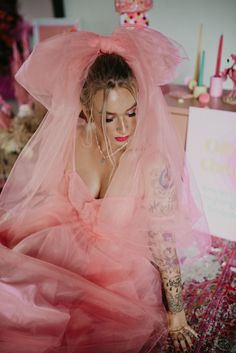 a woman wearing a pink dress and veil sitting on the floor with her hands behind her head