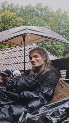 a man with long hair sitting in the back of a truck under an open umbrella