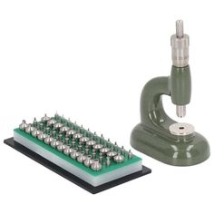 a microscope and some screws on a white surface with a green board in the foreground