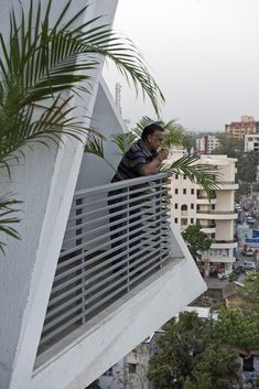 a man standing on top of a balcony next to a palm tree and looking at his cell phone