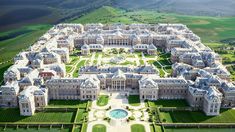 an aerial view of a large white building in the middle of a green field and mountains