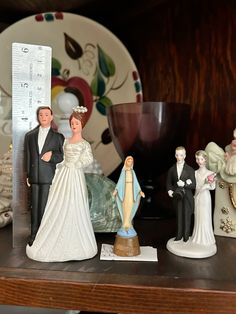 wedding figurines are sitting on a shelf next to a measuring cup and plate