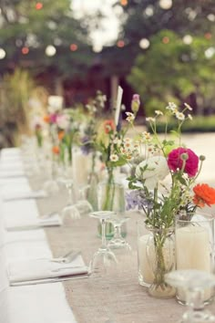 a long table with vases filled with flowers and candles on top of each other