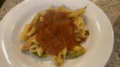 a white plate topped with pasta covered in sauce on top of a marble countertop