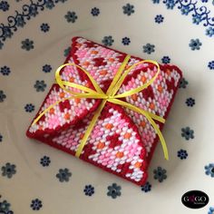 a small red and white box wrapped in yellow ribbon on top of a flowered plate