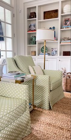 a living room with two green chairs and a white book shelf filled with books on top of it