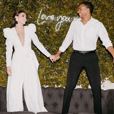 a man and woman holding hands while standing next to a wall with love you written on it