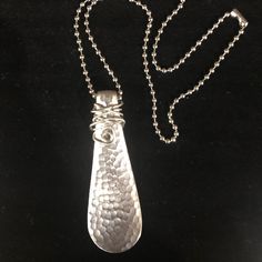 a silver pendant with a chain on a black surface, hanging from it's side