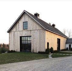 a large wooden building sitting on top of a lush green field next to a gravel road