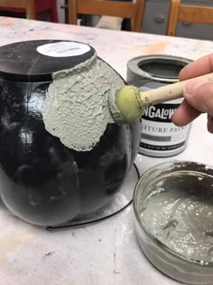 a person is painting a black pot with white paint