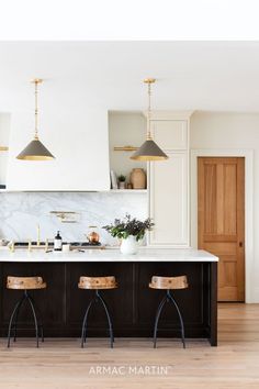 a kitchen with marble counter tops and stools in front of an island that has two pendant lights over it