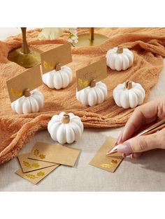 a person is painting small white pumpkins with gold foil on them and place cards in front of them