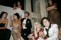 a group of people sitting next to each other in front of a white wall holding drinks