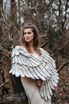 a woman in an angel costume standing next to a tree branch with her wings spread out