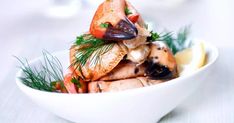 a white bowl filled with seafood and garnished with fresh dill on the side