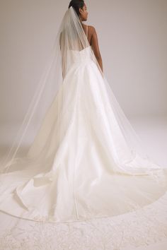 a woman in a wedding dress with a veil on her head is looking back at the camera