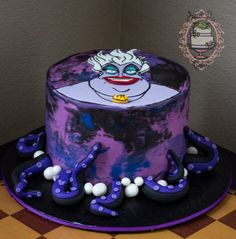 a purple and black cake with an evil clown face on it's top, sitting on a checkered tablecloth