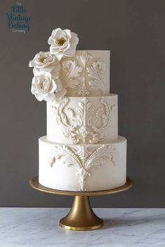 a three tiered white wedding cake with flowers on the top and bottom, sitting on a gold plate