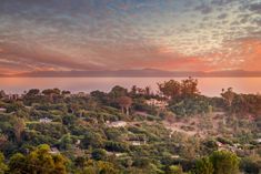 the sun is setting over some trees and houses on a hill with mountains in the background