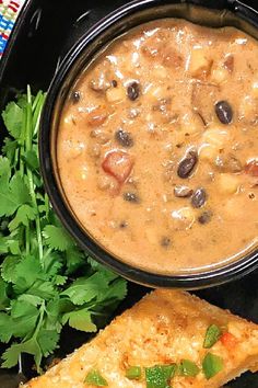 a black plate topped with two pieces of bread and a bowl filled with beans next to some cilantro