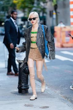 a woman walking down the street in tights and boots with a leather jacket over her shoulders