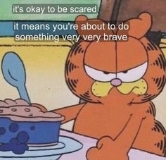 garfield the cat sitting at a table with a cake in front of him and caption that reads, it's okay to be scared it means you're about to do something very brave