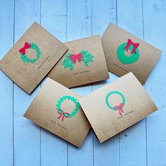 four brown envelopes with christmas stickers on them sitting on a blue wooden surface