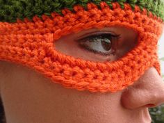 a close up of a person wearing a crocheted orange and green face mask