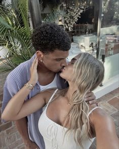 a man and woman kissing in front of a store window with palm trees behind them