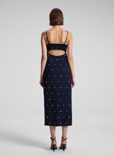 The Alana Dress combines deep rich navy cady fabric and black high-shine satin, adorned with scattered, teardrop-shaped crystals, offering a unique take on festive embellishment. This midi silhouette features a straight skirt, a bustier-inspired bodice with adjustable straps, and delicate side cutouts with an open back for a modern, striking look. Shop Dresses. Styling Tip: Pair with metallic heels and a sleek clutch for an elegant dinner or holiday soirée. Holiday Soiree, Evening Midi Dress, Shaped Crystals, Embellished Midi Dress, Elegant Dinner, Metallic Heels, Straight Skirt, Black Crystals, Shop Dresses