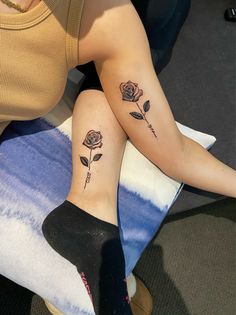 two women with matching tattoos on their legs sitting next to each other, one has a rose and the other has an arrow